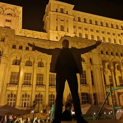 DJ Florin Popescu cu brațele desfăcute în fața Palatului Parlamentului din București, la un eveniment în aer liber