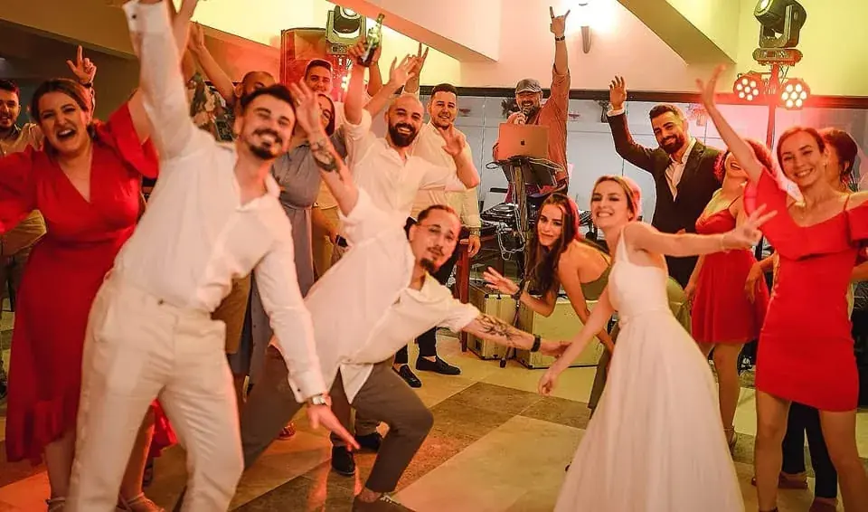 Mireasa și invitații dansează cu mâinile sus la o nuntă, cu DJ Florin Popescu la pupitru în spate